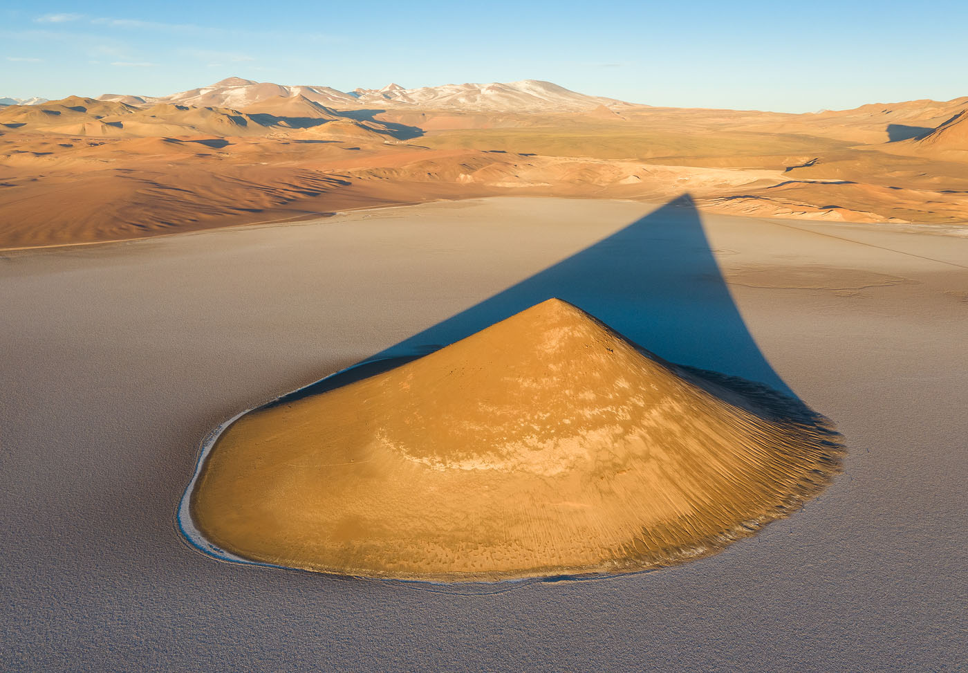 The Argentinean high–altitude desert is a vast, amazing, less photographed place. Even a prominent, ultra–photogenic location like Cono Arita (shown here) had yet to be photographed with a drone when I got there – and so I took the opportunity to create something new, and hopefully appealing. I took a few shots before sunrise, but the main event was once the sun rose sufficiently high for the shadow to appear fully on the salt pan.  <br>DJI Mavic II Pro, f/8, 1/60 sec, ISO 100 <br>Cono Arita, Puna de Argentina