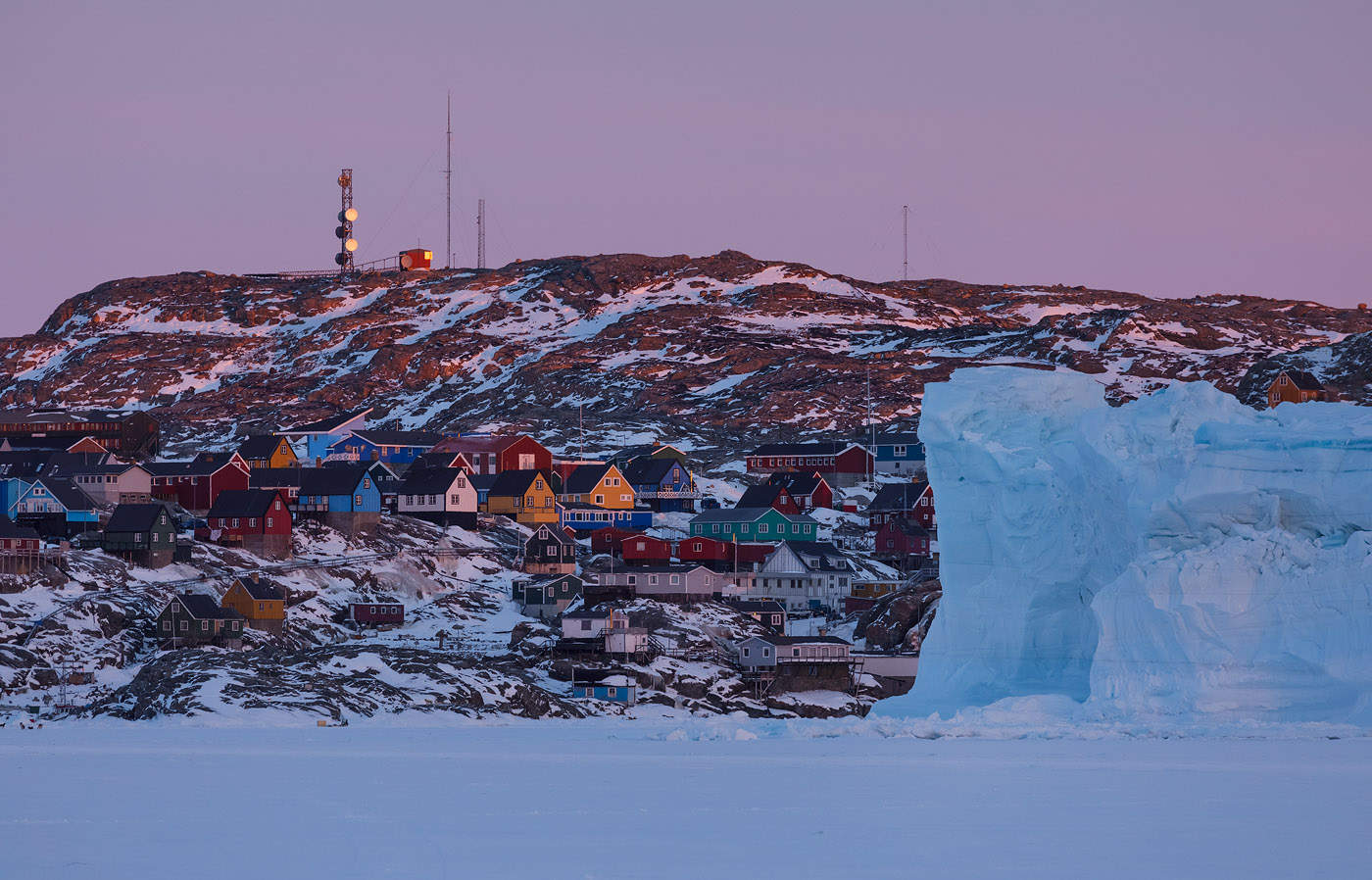 Houses in Uummannaq and an iceberg stuck in sea ice next to town