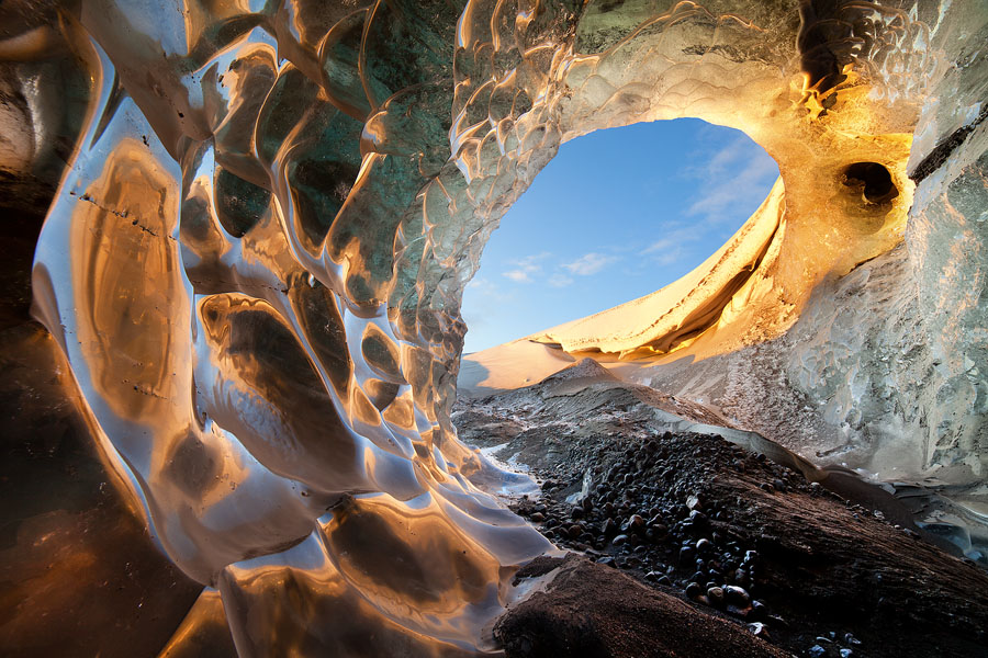 The sun, reflected on the walls of this ice cave, is what caused it to form. This image tells the story of the glacial melting, and the inclusion of the cause and its effect enriches the picture's visual appeal.